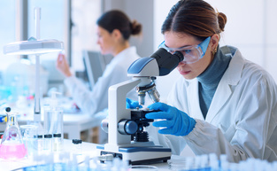 Young scientists conducting research investigations in a medical laboratory, a researcher in the foreground is using a microscope